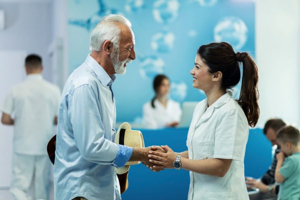 Happy senior man handshaking with female doctor while talking in lobby at clinic.