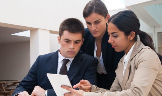 Serious woman showing tablet screen to business people. Business man and women discussing issues, standing and sitting at cafe table. Order concept. Front view.