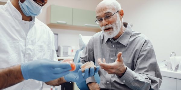 Handsome old man talking to the dendist. Two men in the dentist's office. The doctor shows the patient dentures
