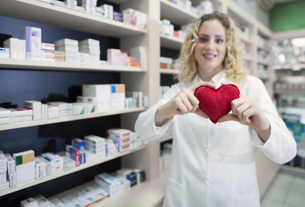 Female pharmacist holding heart and promoting cardiovascular medications and successful treatment.