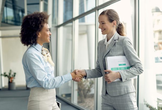 Happy businesswoman and her black female colleague shaking hands in a lobby.
